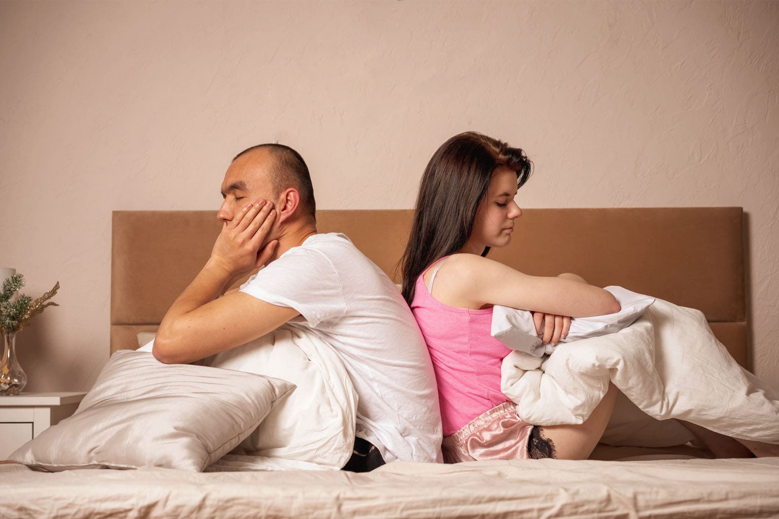 Couple dans un lit dos à dos avec des oreillers, illustrant la baisse de libido et les tensions dans le couple liées à la charge mentale et à la fatigue du quotidien.
