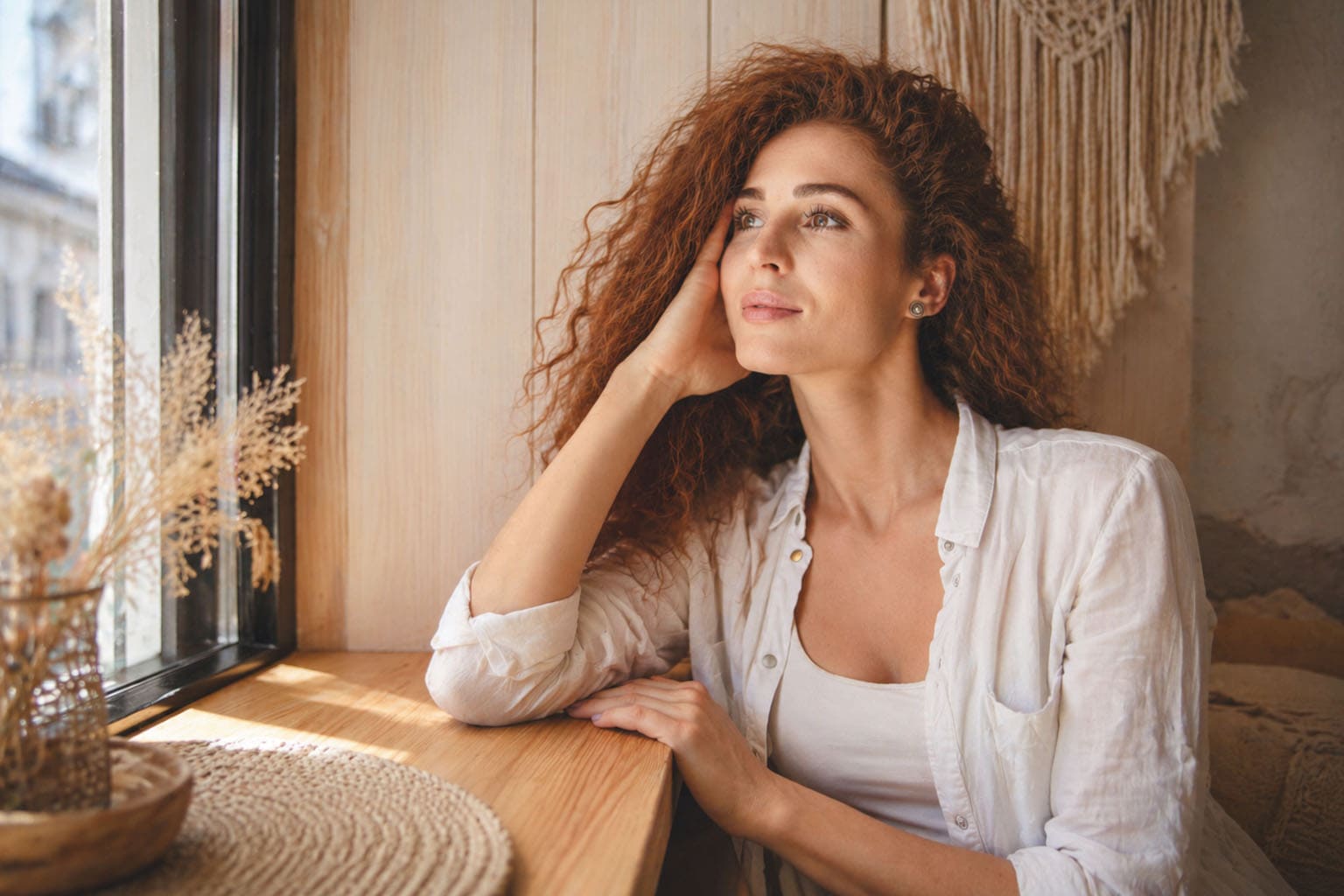 Femme pensive regardant par la fenêtre, incarnation de la charge mentale d’une maman active au quotidien